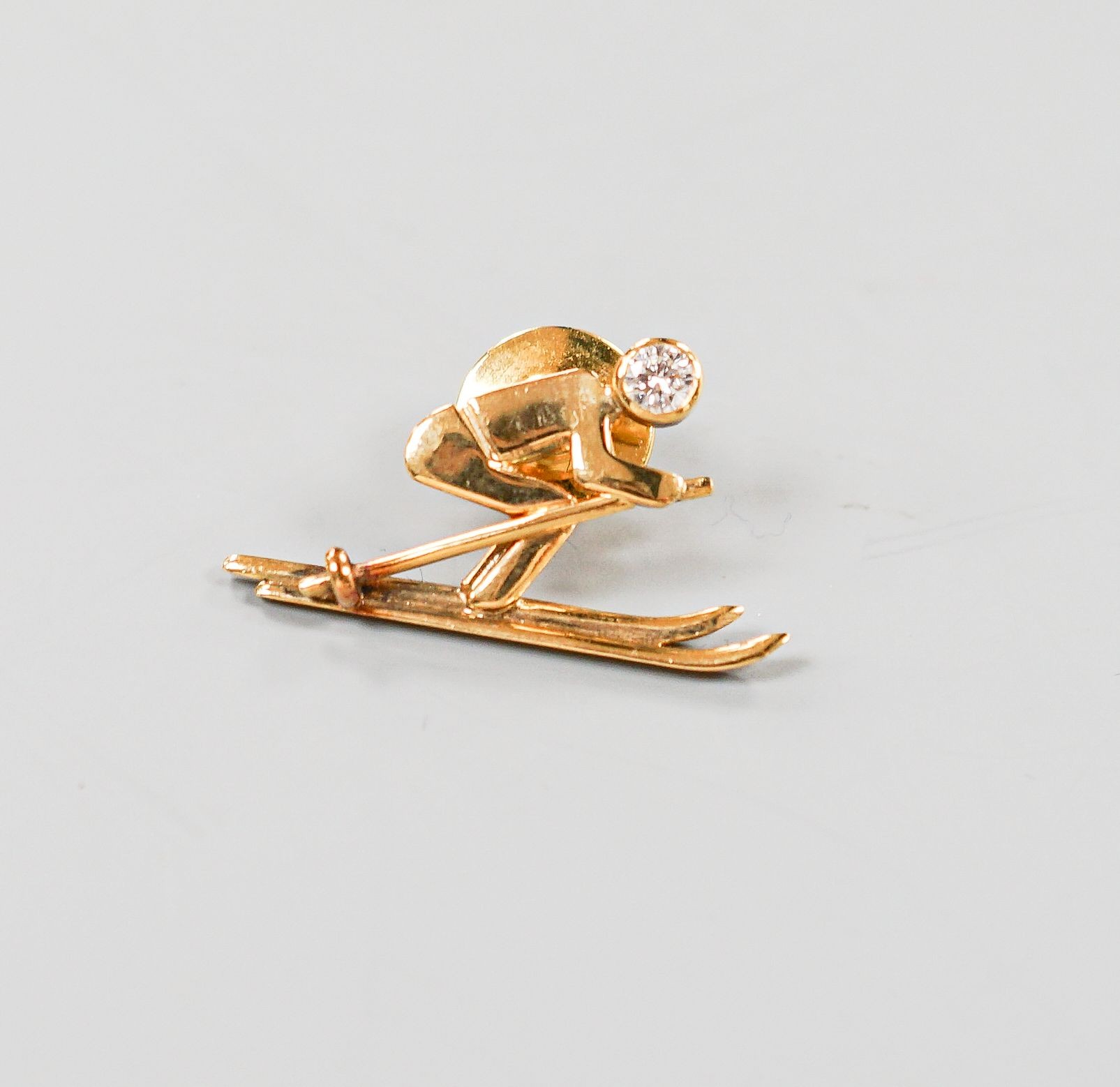 A yellow metal and single stone diamond set dress stud?, modelled as a skier, 31mm, gross 4.5 grams.